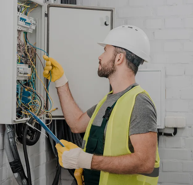 Électricien en train de réparer un tableau électrique avec équipement de sécurité.
