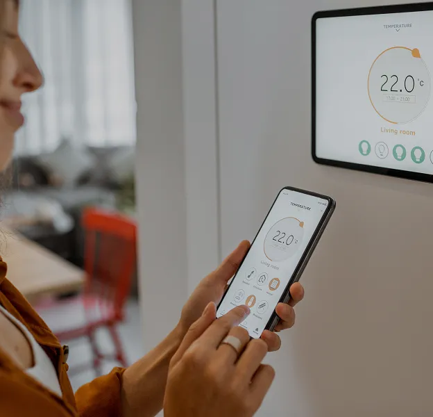 Personne vérifiant température ambiante 22.0°C sur smartphone et écran mural.