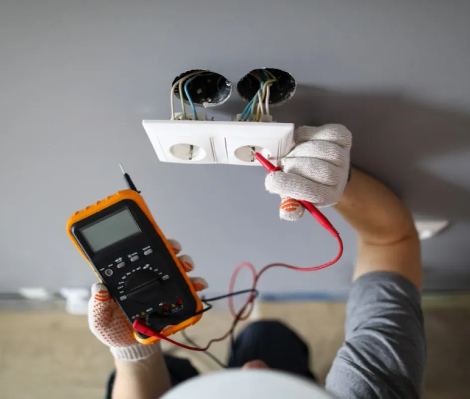 Technicien vérifie tension électrique avec multimètre sur double prise murale.