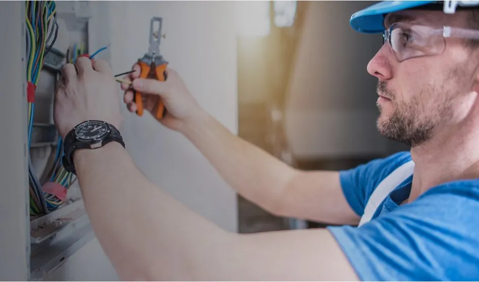 Électricien en train de réparer un tableau électrique avec des outils.