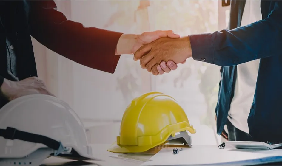Électricien serrant la main d'un client avec casques de chantier en arrière-plan.