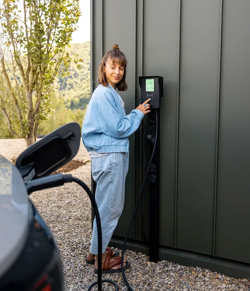 Femme branchant voiture électrique à une borne de recharge extérieure.
